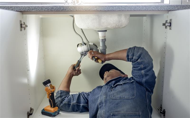 Plumber repairing pipes beneath a bathroom sink in San Juan Capistrano